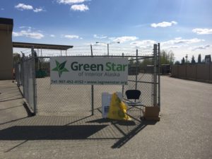 A large white sign attached to a chain link fence reads "Green Star of Interior Alaska." The chain link fence is enclosing a flat paved area.
